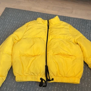 Gul pufferjacka från H&M Divided - Säljer en riktigt fet gul pufferjacka från H&M Divided i storlek 36. Jackan har svart dragkedja, två stora fickor fram och snörning vid midjan. Perfekt för dig som vill sticka ut med en färgglad look under kalla dagar. Jackan är långärmad och har en schysst loose passform.