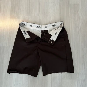 Bruna Dickies 874 shorts W32 - Snygga bruna shorts från Dickies, modell 874 Original Fit. Klassisk rak passform med råa kanter nertill för en avslappnad vibe. Tillverkade i slitstark bomull/polyester-mix, perfekta för sommardagar. Ikonisk logga på insidan av linningen.