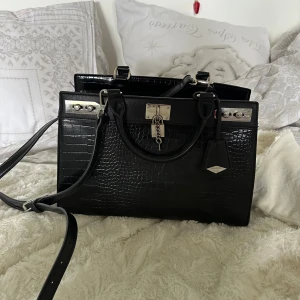 Svart axelremsväska - Snygg axelremsväska i skinnimitation från Aldo. ❤️ Har avtagbara axelband ifall man hellre vill använda som handväska, och 3 innerfickor. I perfekt skick då den är varsamt använd. Perfekt för skola eller vardagligt bruk! 