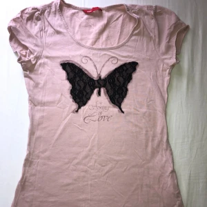Ljusrosa t-shirt med spetsfjäril från edc - Söt ljusrosa t-shirt från edc med korta ärmar och rund halsringning. Framsidan pryds av en stor svart fjäril i spetsmaterial.