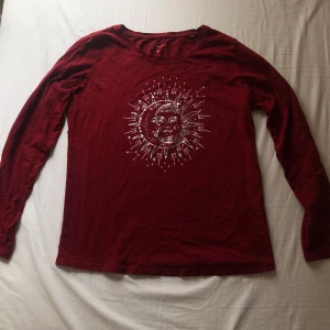 Röd långärmad tröja med sol- och måntryck - Röd långärmad tröja med ett tryck av sol och måne. Rund halsringning och mjukt bomullsmaterial. 