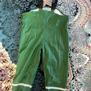 Säljer ett par gröna täckbyxor från Exani med justerbara svarta hängslen och reflexdetaljer vid benen. Perfekta för utomhuslek under kalla och blöta dagar. Vattentätt material som håller dig torr. För barn.