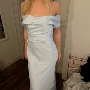 Ljusblå axelbandslös långklänning - Säljer en elegant ljusblå långklänning med offshoulder-design och figurnära passform. Klänningen har en vacker drapering över bysten och en diskret dragkedja i ryggen. Perfekt för bal eller festliga tillfällen. Jag säljer den för att den helt enkelt var för stor för mig men den är min dröm klänning