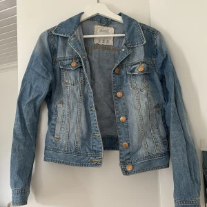  blå jeansjacka  - Säljer en blå lite tajtare jeansjacka med guldiga knappar och två bröstfickor. Jackan har lång ärm, krage och snygga sömdetaljer. Är i storlek 38 men skulle säga att den passar 36 bättre 