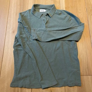 Grön pikétröja med lång ärm - Säljer en stilren grå pikétröja med lång ärm och klassisk krage. Tröjan har knappar framtill och är tillverkad i ett mjukt material som passar perfekt till vardags. 