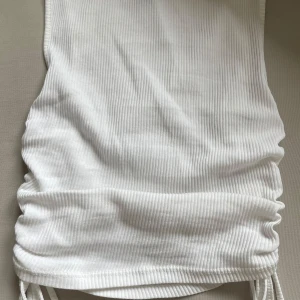 Vit ribbad croppad linnetopp från H&M Divided - Säljer en vit ribbad linnetopp från H&M Divided i storlek XS. Toppen är croppad och har en justerbar snörning i sidorna som ger en cool känsla. Perfekt för varma dagar och enkel att matcha med vilken outfit som helst. Den är väldigt liten i storleken, men ganska stretchig. 
