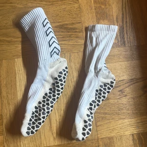 Vita skillsocks med svart mönster från Hummel - Säljer ett par vita träningsstrumpor från Hummel med svarta pilar på skaftet och svarta gummigrepp under foten. Strumporna är ribbade upptill och har en sportig look, perfekta för inomhusträning eller fotboll.
