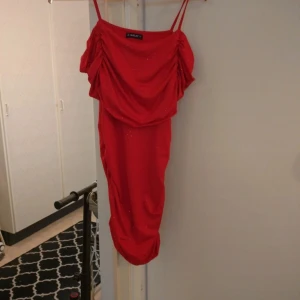 Röd glittrig klänning från Sheilay - Säljer en röd, glittrig klänning från Sheilay med smala axelband och draperad framsida. Klänningen är kort och har en figurnära passform, perfekt för att sticka ut. Snygg detalj med små glittrande stenar över hela tyget.