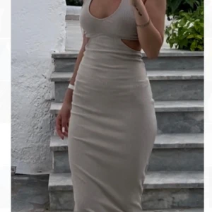 Beige ribbad långklänning med cut out - Säljer en beige ribbad långklänning med rund ringning och cut out-detalj vid midjan. Klänningen är ärmlös och har en tight passform som framhäver figuren. Perfekt för sommarens alla tillfällen!