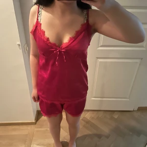 Rosa satinlinne med spetsdetaljer och pyjamas shorts  - Säljer ett glansigt rosa linne i satin med tunna axelband och spetsdetaljer längs urringningen. Och ett par pyjamas shorts nästan aldrig använda Linnet har en liten rosett framtill och är perfekt för mysiga hemmakvällar.