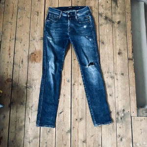 Blå Replay jeans med slitningar - Säljer ett par blå jeans från Replay med snygga slitningar och hål på ena benet. Klassisk femficksmodell med raka ben och normal passform. Säljer pga att de blivit för små. Perfekta för en avslappnad stil. 