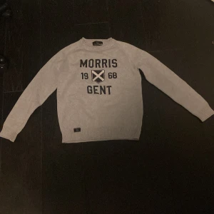Ljusgrå tröja från Morris Gents - Säljer en ljusgrå tröja från Morris Gents med svart tryck framtill där det står 'Morris Gent 1968' och ett emblem. Tröjan har rund halsringning och långa ärmar, samt ribbade muddar vid ärmslut och nederkant.