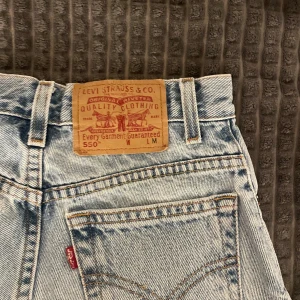 Levi's ljusblå jeansshorts med fransar - Klassiska ljusblå jeansshorts från Levi's med råa franskantade benslut och femficksmodell. Shorts med hög midja och ikonisk läderpatch baktill. Perfekta för sommaren och enkel att matcha med allt.