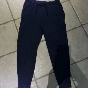 Mrökblåa mjukisbyxor från Nike - Säljer ett par mörkblåa mjukisbyxor från Nike i storlek M. Byxorna har dragsko i midjan och ribbade muddar vid bensluten. Klassisk Nike-logga på benet och mjukt material som passar perfekt för en avslappnad stil.