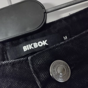 Svart jeanskjol från BikBok - Svart jeanskjol från BikBok med slitna detaljer framtill och rå kant nedtill. Femficksdesign och knappstängning.