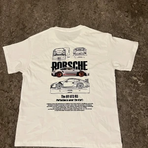 Vit Porsche 911 GT3 RS t-shirt - Vit t-shirt med stor Porsche 911 GT3 RS-illustration och text på ryggen. Trycket visar olika vyer av bilen och har svarta och röda detaljer. Framsidan är helt vit utan tryck. Perfekt för bilentusiasten!