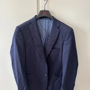Mörkblå kavaj från Dressmann - Säljer en stilren mörkblå kavaj från Dressmann i slim fit-modell. Kavajen har två knappar framtill, klassisk krage och innerfoder i ljusblått. Perfekt för dig som vill ha en enkel och snygg look.