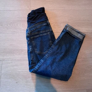 Mammabyxor i blå denim - Säljer ett par blå mammabyxor i jeansmaterial med mjuk, svart stretchpanel över magen. Klassisk femficksmodell och raka ben. Perfekta för dig som vill ha bekväma jeans under graviditeten.