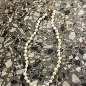 Pärlhalsband med gulddetaljer - Elegant halsband med vita pärlor och små guldfärgade detaljer mellan varje pärla. Justerbart lås i guldton. Perfekt för att lyfta vilken outfit som helst.