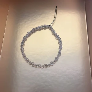 Genomskinligt pärlarmband - Säljer ett enkelt och stilrent armband med genomskinliga pärlor. Armbandet har en tunn svart tråd som knyts för att justera storleken. Perfekt accessoar för att ge en diskret touch till din outfit.