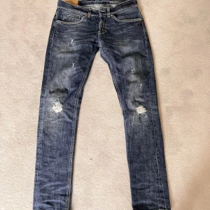 Blå slitna jeansbyxor från dondup - Säljer ett par blå jeansbyxor från dondup med slitna detaljer och hål på båda knäna. Modell: George. Storlek 32
