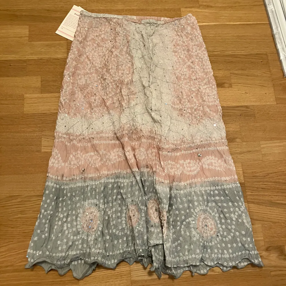 Säljer en bohemisk långkjol från Indiska i ljusrosa och grå toner med subtilt batikmönster. Kjolen har paljettdetaljer som ger extra glans och ett vågigt avslut nertill. Perfekt för dig som gillar en unik och luftig stil.. Hameet.