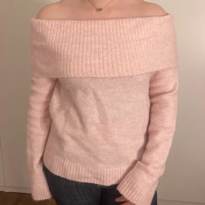 Ljusrosa offshoulder stickad tröja - Mysig ljusrosa stickad tröja med bred ribbad offshoulder-krage. Tröjan har lång ärm och är perfekt för dig som vill ha en feminin och trendig look. Passar snyggt till både jeans och kjol.