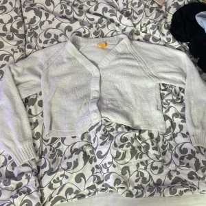 Vit croppad kofta från Gina Tricot - Säljer en vit croppad kofta från Gina Tricot. Koftan har långa ärmar, v-ringning och knäpps med tre vita knappar framtill. Perfekt att slänga över en topp för en enkel och stilren look.