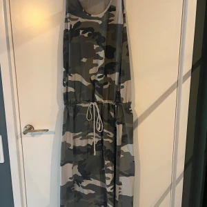Långklänning med camouflage-mönster - Säljer en ärmlös långklänning med camouflage-mönster och knyt i midjan. Klänningen har rund halsringning och är perfekt för dig som gillar en avslappnad och cool stil. 97 % bommul och 3% elastin. Kommer från märket sixty days. Köpt i liten butik på Gotland. Nypris 1200 kr