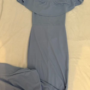 Ljusblå offshoulder långklänning - Säljer en elegant ljusblå långklänning med offshoulder-design och volang upptill. Klänningen har en smickrande passform och är perfekt för speciella tillfällen. Materialet känns mjukt och följsamt.