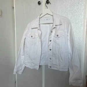 Vit jeansjacka med silverknappar - Säljer en klassisk vit jeansjacka från Monki. Jackan har silverfärgade knappar framtill och på bröstfickorna, samt två sidofickor. Modellen är normal i passformen och har lång ärm. Perfekt att slänga över en t-shirt eller hoodie.