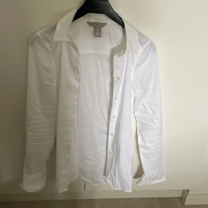 Vit skjorta från H&M - Klassisk vit skjorta från H&M med lång ärm och knäppning framtill. Skjortan har en stilren design med normal passform och mjukt bomullsmaterial. Perfekt till många olika tillfällen.