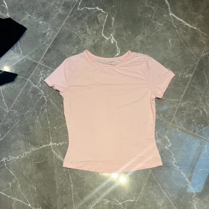 Ljusrosa t-shirt - Säljer en ljusrosa t-shirt med rund halsringning och korta ärmar. Enkel och stilren design som passar perfekt till jeans eller kjol. Supermjuk och skön att ha på sig!