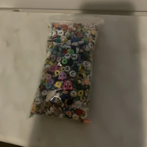 Påse med färgglada pärlor i olika former - En stor påse med blandade pärlor i olika färger och former, inklusive bokstavspärlor och figurer. Perfekt för att skapa egna armband, halsband eller andra smycken. Pärlorna är av plast och kommer i många glada färger.