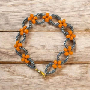 Handgjort armband - Ge din outfit en färgklick och en unik touch med detta handgjorda pärlarmband, dekorerat med ett charmigt blommönster i lysande orange och skimrande grå pärlor. Den lekfulla och iögonfallande designen passar perfekt för att lyfta vardagslooken eller komplettera sommarens stil.