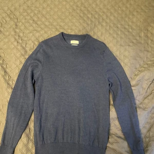 Mörkblå merinoulltröja från These Glory Days - Säljer en stilren mörkblå tröja från These Glory Days i 100% merinoull. Tröjan har rund halsringning och långa ärmar.. Enkel och klassisk design som passar till mycket.