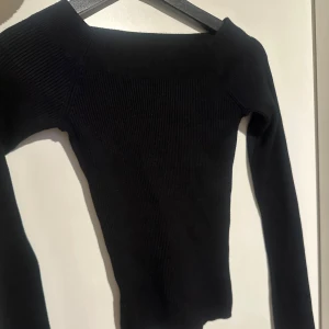 Svart ribbad tröja med bred halsringning - Säljer en svart ribbad tröja med bred halsringning. Tröjan har lång ärm och är figurnära i modellen, perfekt att styla till jeans eller kjol. Enkel och stilren design som passar till mycket.