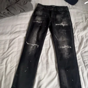 Svarta jeans med slitningar och färgstänk - Säljer ett par svarta jeans med slitningar och coola färgstänk. Jeansen har en slim passform och detaljerade slitningar på både lår och knän för en trendig look och jeansen e från supply demand .