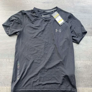 Svart compression shirt från Under Armour - Säljer en svart compression shirt från Under Armour med diskret logga på bröstet och text längs sidan. 