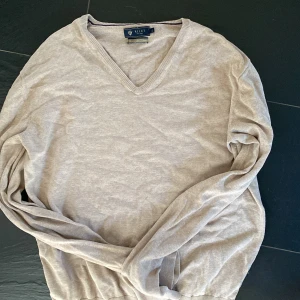 Beige v-ringad tröja från Riley - Säljer en stilren beige v-ringad tröja från Riley. Tröjan har långa ärmar och är tillverkad i ett mjukt bomullsmaterial. Perfekt för lager-på-lager och enkel att matcha med olika outfits. Defekt i högerarmhåla där det krävts lite fix men fungerar utmärkt