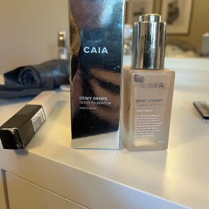 CAIA Dewy Drops Serum Foundation - CAIA Dewy Drops Serum Foundation 20W med vitamin E ger en återfuktande och lystergivande finish. Kommer i en glasflaska med silvrig pump och tillhörande förpackning. Perfekt för dig som vill ha en naturlig glow och jämn hudton. Endast använd 4 gånger 