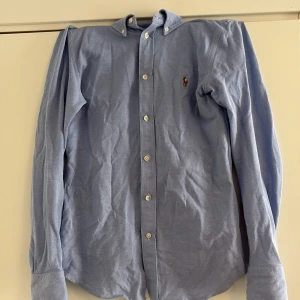 Ljusblå skjorta från Polo Ralph Lauren - Klassisk ljusblå oxfordskjorta från Polo Ralph Lauren med button-down krage och broderad logga på bröstet. 