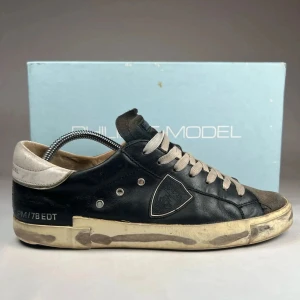 Philippe Model svarta sneakers med vita detaljer - Säljer ett par svarta Philippe Model sneakers med vita snören och detaljer. Skorna har rund tå, platt sula och en ikonisk sköldlogga på sidan. Ovandelen är i skinn med kontrasterande grå och vita partier. Perfekta för en avslappnad streetstil. Skicket är 9/10. Boxen tillkommer. Pris kan diskuteras vid snabb affär. Strl 42 men stora i storleken så passar 43