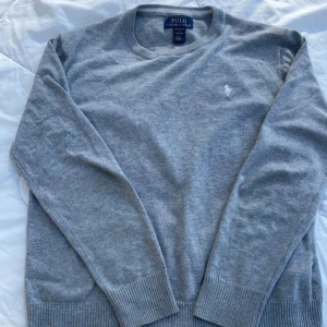 Grå tröja från Polo Ralph Lauren - Säljer en stilren grå tröja från Polo Ralph Lauren i mjuk pima bomull. Tröjan har en broderad logga på bröstet och långa ärmar med ribbade muddar. Perfekt för en avslappnad och klassisk look. Tröjan är i toppen kvalitet och inga skador vad jag vet skriv till mig vid frågor eller vid fler bilder! Kolla min profil för fler feta kläder, kan ordna bra paketpriser! 😊