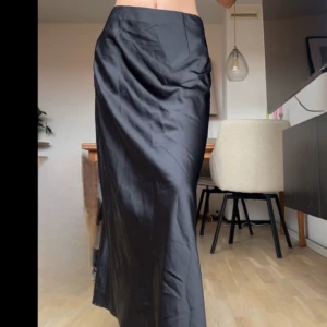 Svart långkjol i satin - Säljer en svart långkjol i glansigt satinmaterial. Kjolen har en rak passform med slits på sidan. Från BikBok! Är 160 och har strl XS (använd fåtal ggr)