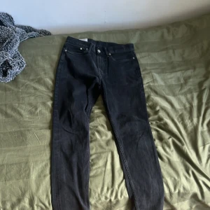 Svarta jeansbyxor - Säljer ett par svarta jeansbyxor med klassisk femficksdesign och raka ben. Byxorna har knapp och dragkedja framtill samt bälteshällor. Perfekta till många olika outfits.