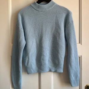 Ljusblå stickad tröja från FB Sister - Säljer en ljusblå stickad tröja från FB Sister. Tröjan har en högre ribbad krage och långa ärmar. Den är mjuk och har en klassisk, enkel design som passar perfekt till jeans eller kjol.