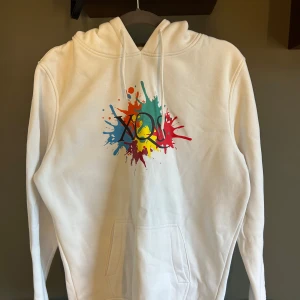Vit hoodie från XQS  - Vit hoodie från XQS med färgstänk-tryck framtill och texten 'MADE BY SWEDEN' på ärmen tillsammans med svensk flagga. Mjuk och skön med känguruficka och huva. Vann på en tävling på xqs