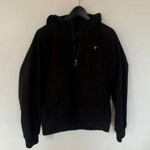 Svart vindjacka Lyle & Scott - Softshell jacka från Lyle & Scott med huva och dragkedja framtill. 