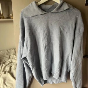 Ljusblå stickad tröja från Gina Tricot - Mysig ljusblå stickad tröja från Gina Tricot med krage och långa ärmar. Tröjan har en avslappnad passform och ribbade detaljer vid nederkant och ärmslut. Perfekt för kyliga dagar!